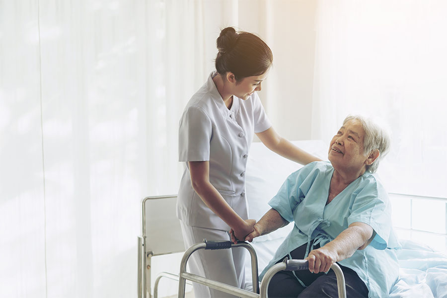 Caregiver assists elderly patient with walker.