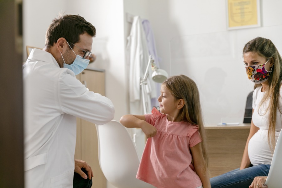 Masked doctor bumping elbows with young patient
