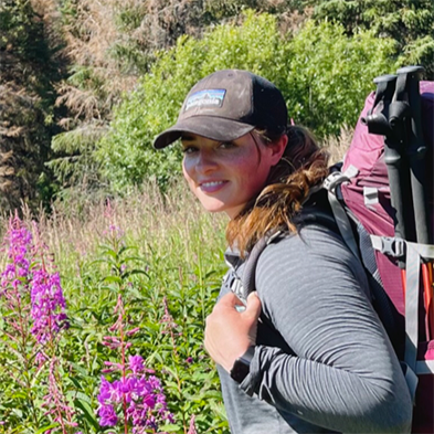 Laura Morgan backpacking through a field with flowers in bloom