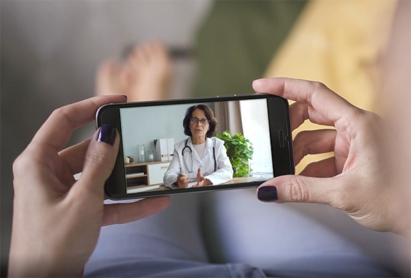 Hands holding mobile phone showing doctor on telehealth call