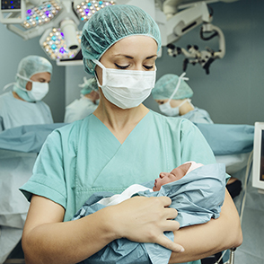 Caregiver in scrubs holding swaddled newborn baby