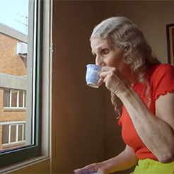 Elderly woman sipping tea while looking out apartment window