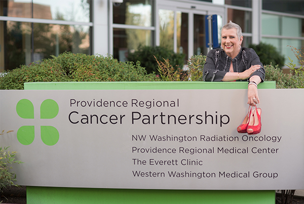 Mollie Marie dangles a pair of red high heels in front of the Providence Regional Cancer Partnership sign