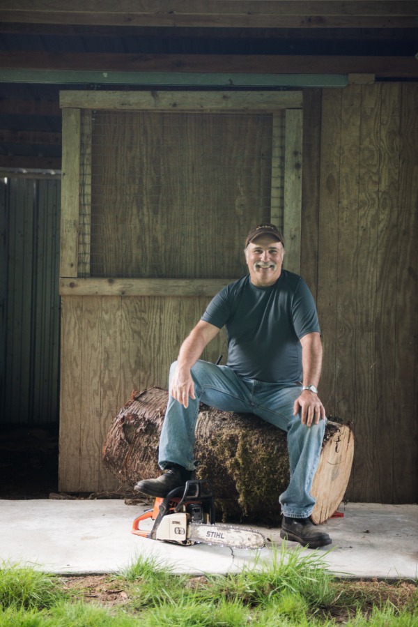 George Schlosser sitting on cut log with chainsaw at his feet