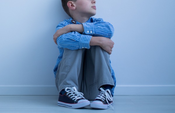 Young boy sits alone with back against a wall.