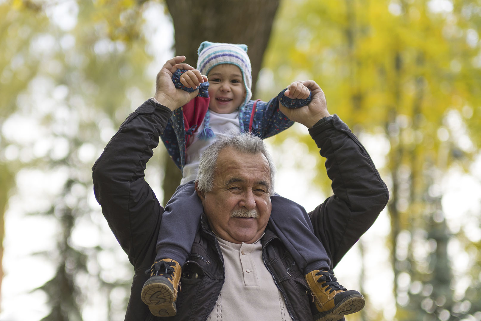 older man with small child on his shoulders both smiling and looking at camera