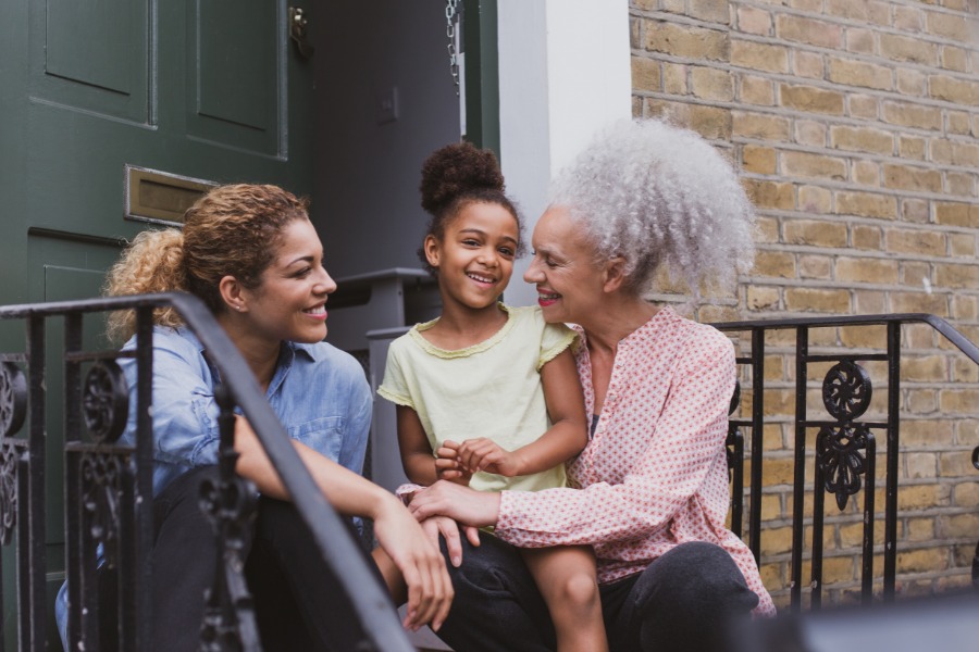 Grandmother, mother, and daughter sitting on housesteps