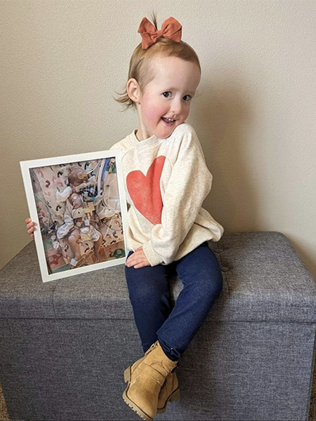 Abigail is 2! Toddler girl holding picture of infant self in NICU.