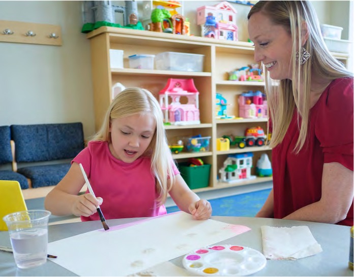 Art therapist watches young girl paints with watercolors