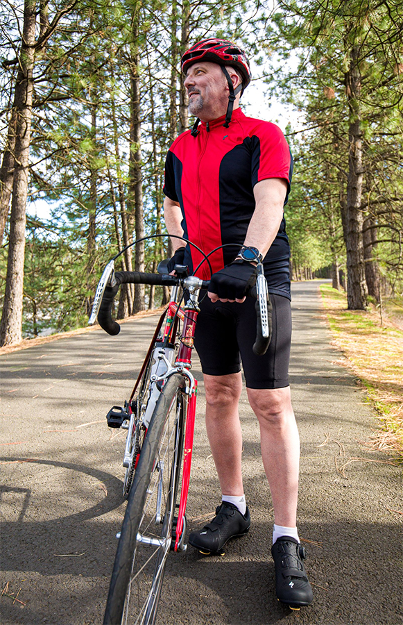 Brian Starr standing next to road bike on wooded path