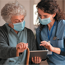 Elderly female patient and caregiver look at tablet device.