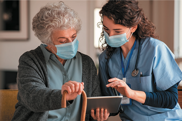 An elderly woman and caregiver look at a tablet together.