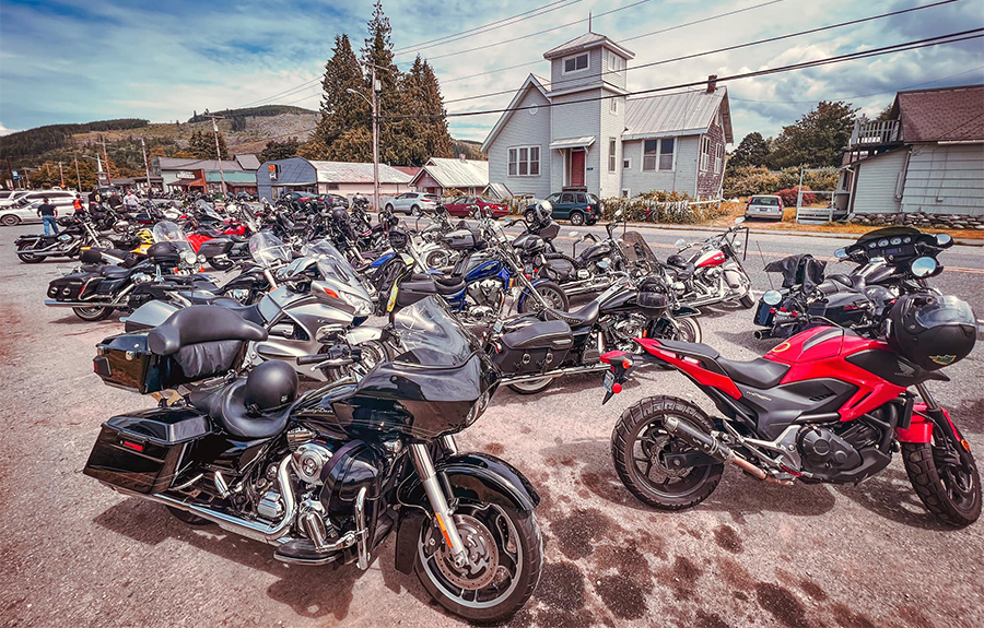 Dozens of parked motorcycles on a dusty roadside with a blue sky in the background.