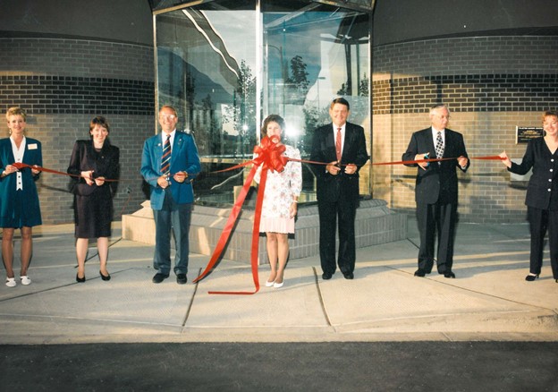 Seven men and women sand behind large red ribbon at ribbon cutting ceremony