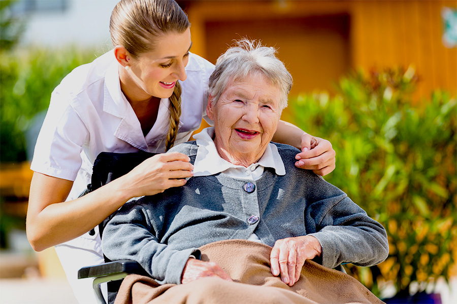 Caregiver pushing elderly woman in wheelchair.
