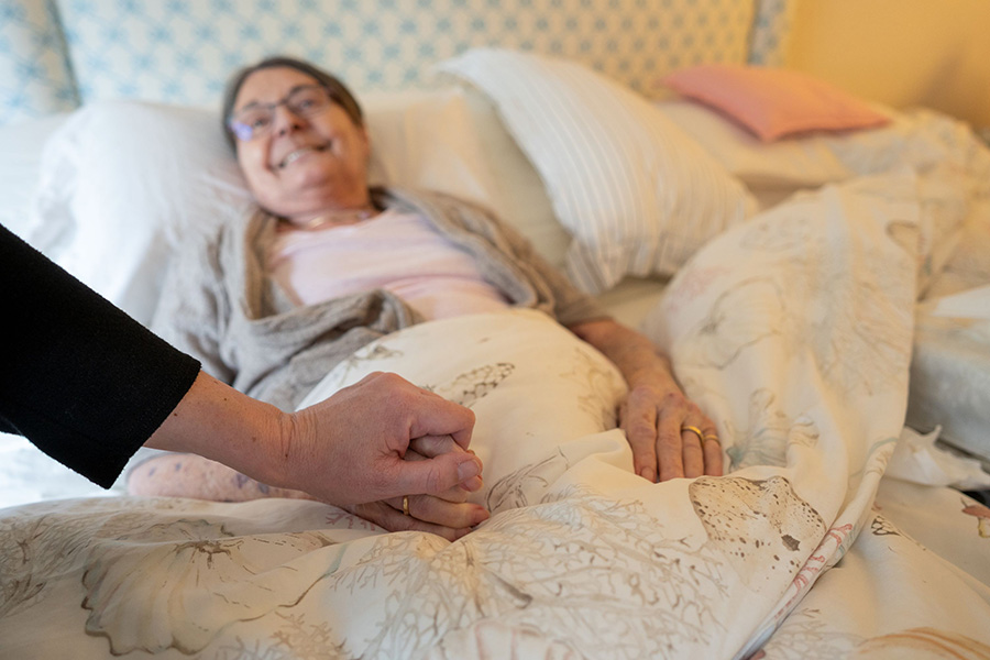 Woman laying in bed holding another's hand.