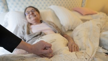 Woman lying in bed while a hand holds hers.