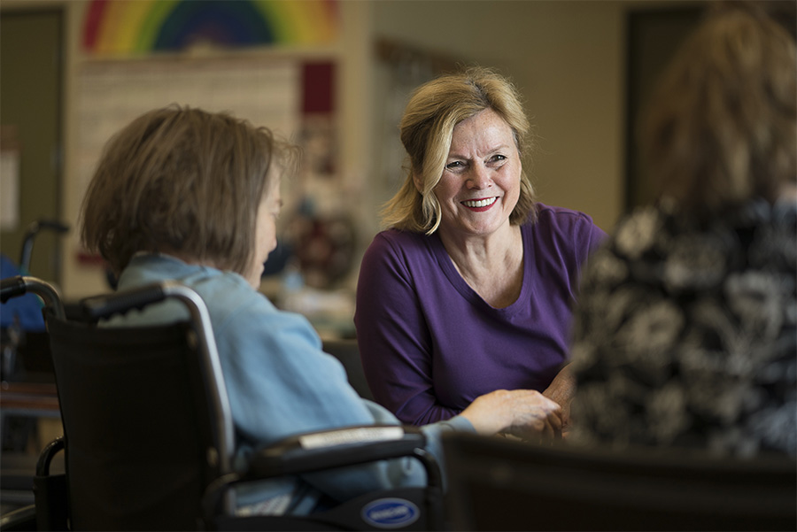 Volunteer Woman talking to two elderly women in wheelchairs.
