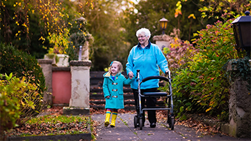 Elderly woman using walker holds hands with preschooler on a park walk in fall