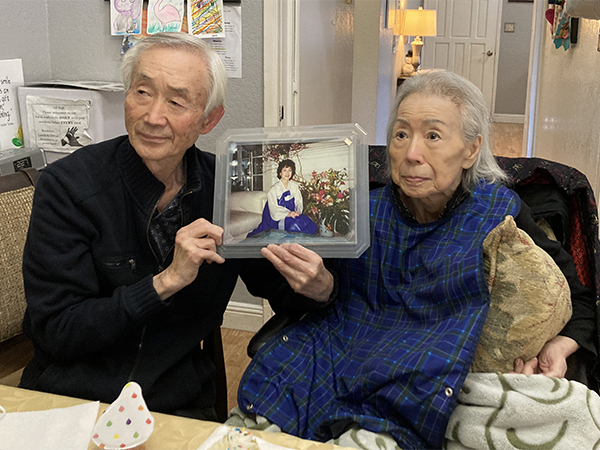 Elderly woman and man hold up photo of woman in younger years